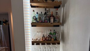 A bar area with shelves of liquor bottles and glasses, a mini-fridge, and a trash can.