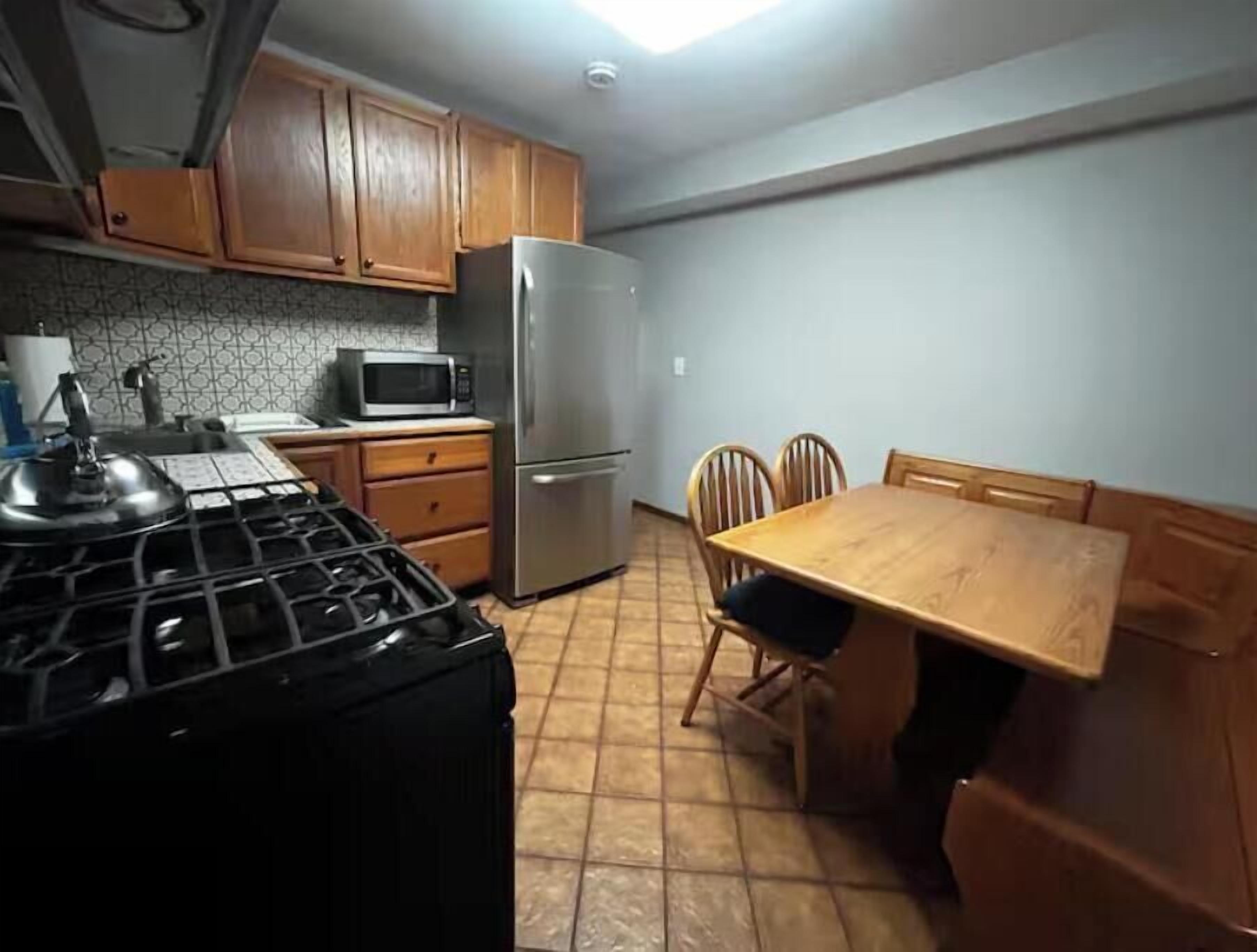 Una cucina con mobili in legno, un frigorifero in acciaio inossidabile, un forno a microonde, un fornello e un tavolo da pranzo con sedie.