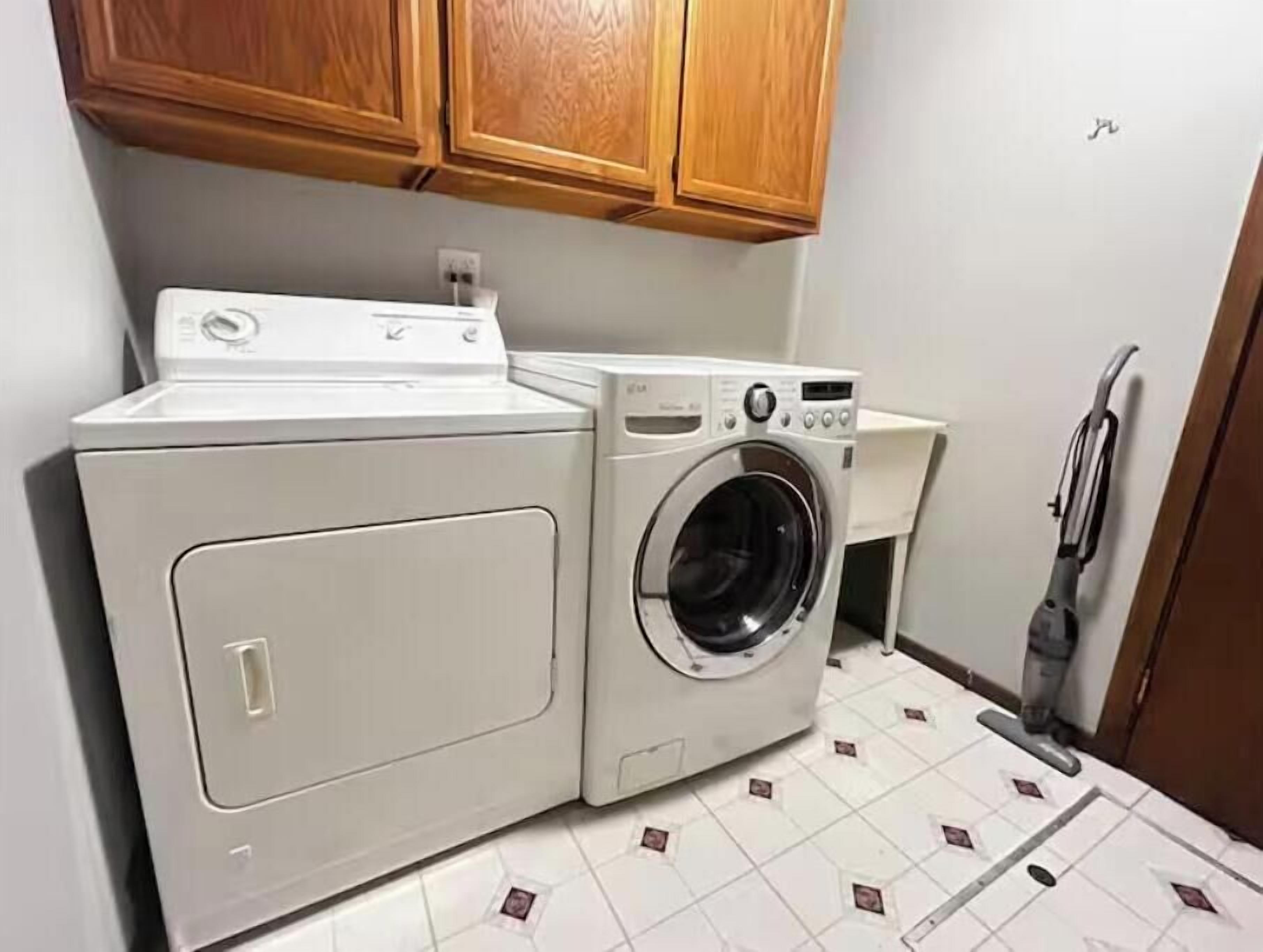 A compact laundry area with a front-loading washer and dryer, wooden cabinets above, and a tiled floor.