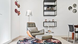 A modern living room with a grey armchair, a matching ottoman, a floor lamp, a round coffee table, and a bookshelf.