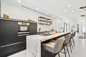 A modern kitchen with a marble island, dark cabinetry, and a dining area with bar stools. - 2BR Getaway | Fully Equipped, AC & Beach Access (Noord)