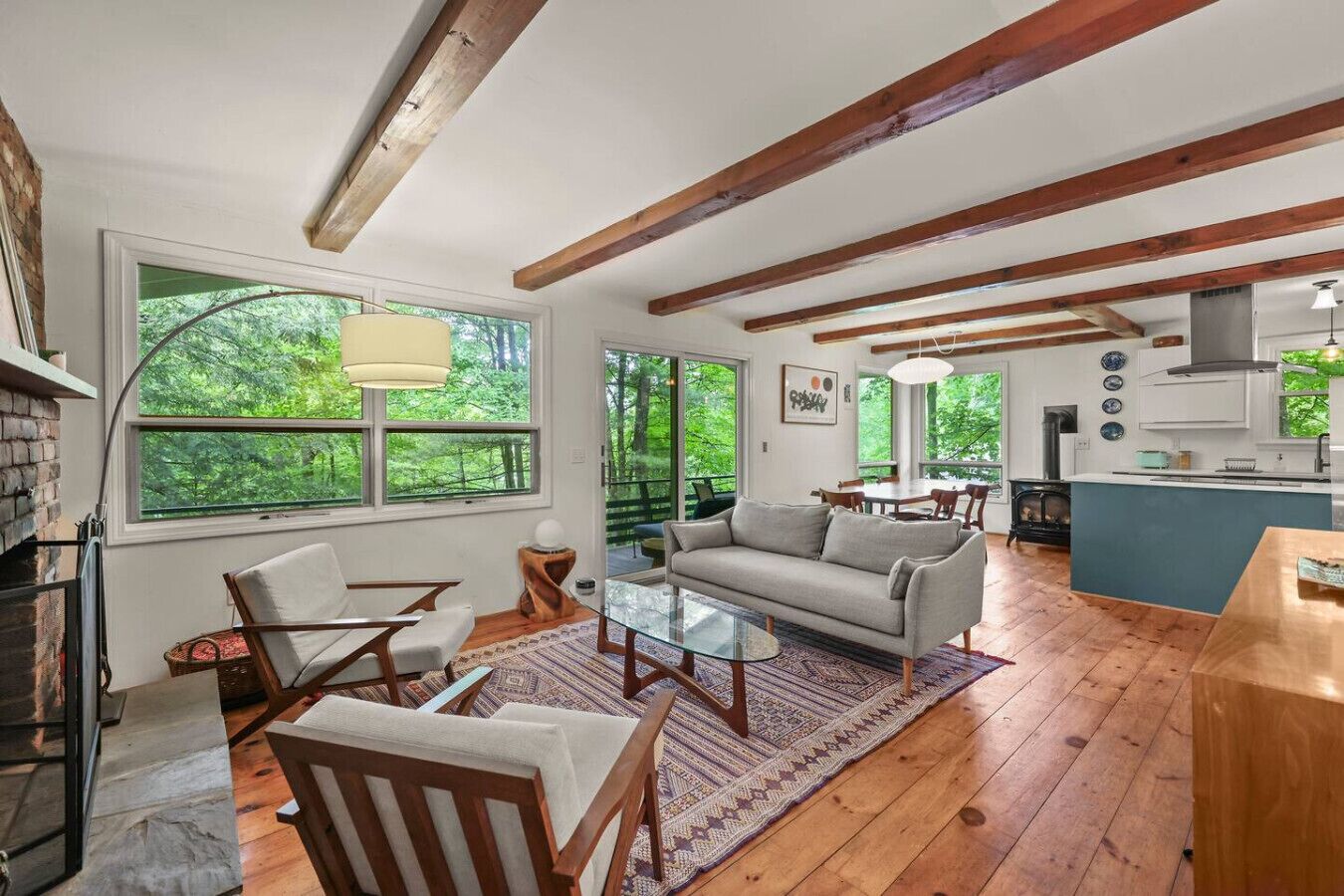 A spacious living area with a fireplace, large windows, a dining table, and a kitchen area.