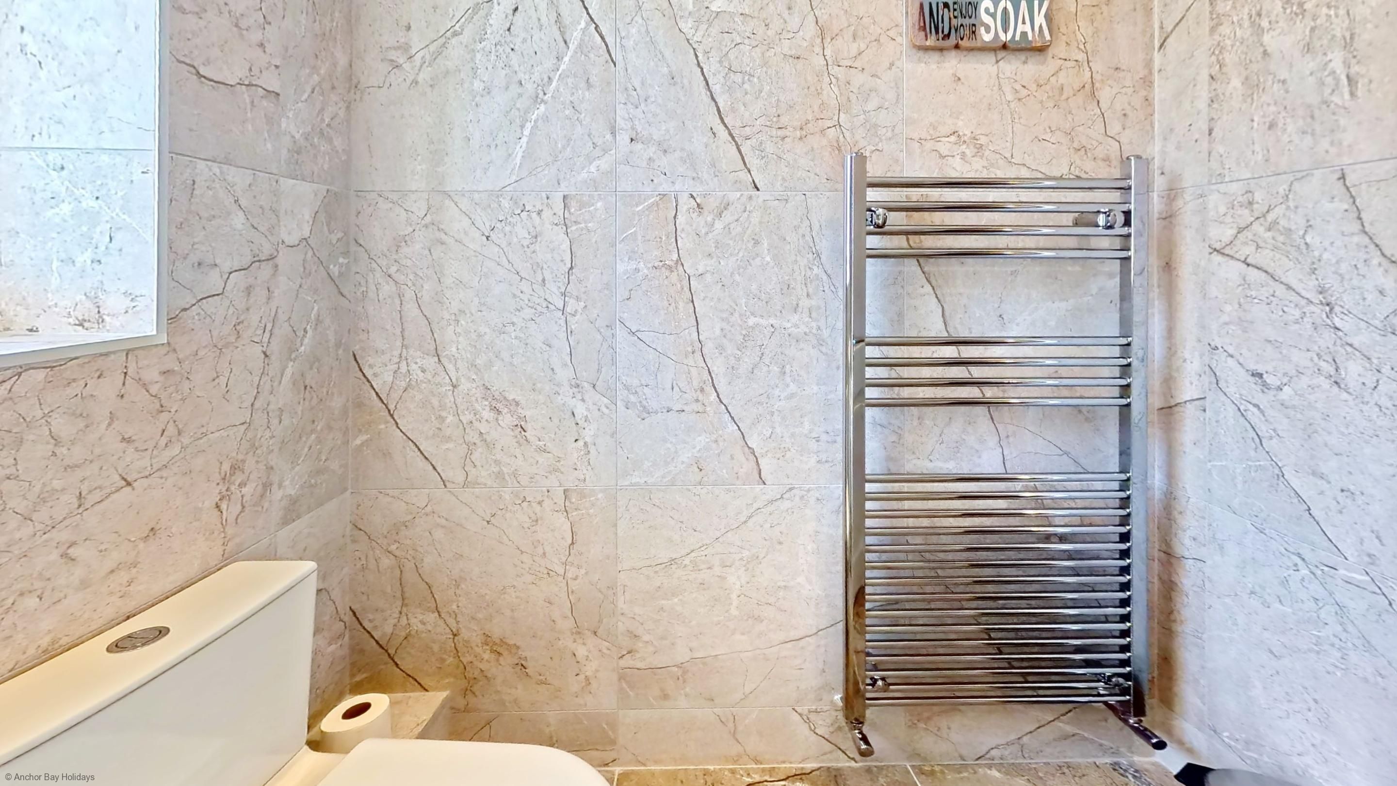 Et badeværelse med marmorvægge, et kromhåndklædestativ og et toilet.