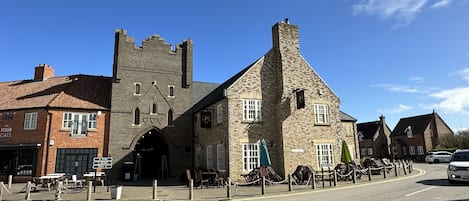 Een historisch gebouw met een opvallende toren en een rondbogening aan een straathoek, met terrasplekken.