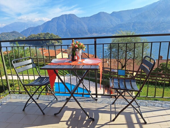 Un balcon avec une table dressée pour deux personnes, offrant une vue sur un paysage montagneux et un plan d’eau.