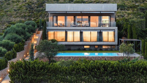 A modern two-story house with a balcony, a swimming pool, and lush greenery.
