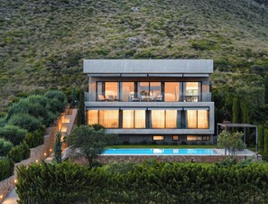 A modern two-story house with a balcony, a swimming pool, and lush greenery. - EXCLUSIVE VILLA WITH BREATHTAKING VIEWS OF THE BAY OF PUERTO POLLENSA (Port de Pollença)