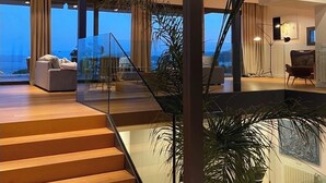 A modern interior with a wooden staircase, glass railings, and a view of the ocean.