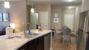 A modern kitchen with a dishwasher, double sink, and a dining area with a table and chairs. - Executive 1st Floor 2BR Dublin Area W D Gym (Dublin)