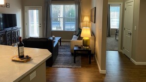 A living room with a sofa, a coffee table, and a TV. There is a window with curtains and a lamp on a side table. - Executive 1st Floor 2BR Dublin Area W D Gym (Dublin)
