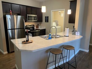 A modern kitchen with stainless steel appliances, a central island with stools, and pendant lighting. - Executive 1st Floor 2BR Dublin Area W D Gym (Dublin)