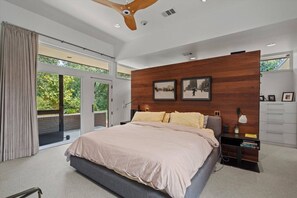A modern bedroom with a large bed, a wooden accent wall, and a view through glass doors.