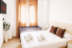 Hotellihuone, jossa on sänky, yöpöytä, lamppu, televisio ja ikkuna, jossa on verhot.