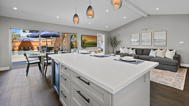 A spacious kitchen with a large island, modern pendant lights, and a view of the outdoor patio area. - Pacific Beach Retreat Coastal Getaway w/ Pool (San Diego)