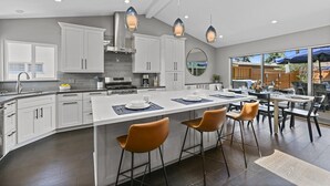 A modern kitchen with white cabinets, a large island, and pendant lighting. - Pacific Beach Retreat Coastal Getaway w/ Pool (San Diego)
