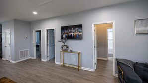 A spacious living area with hardwood flooring, a dark-colored sofa, and a framed cityscape painting on the wall.