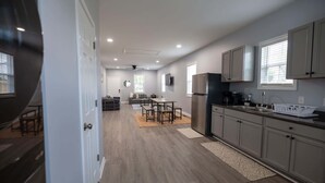 A modern kitchen with grey cabinets, a stainless steel refrigerator, and a dining area with a table and chairs.