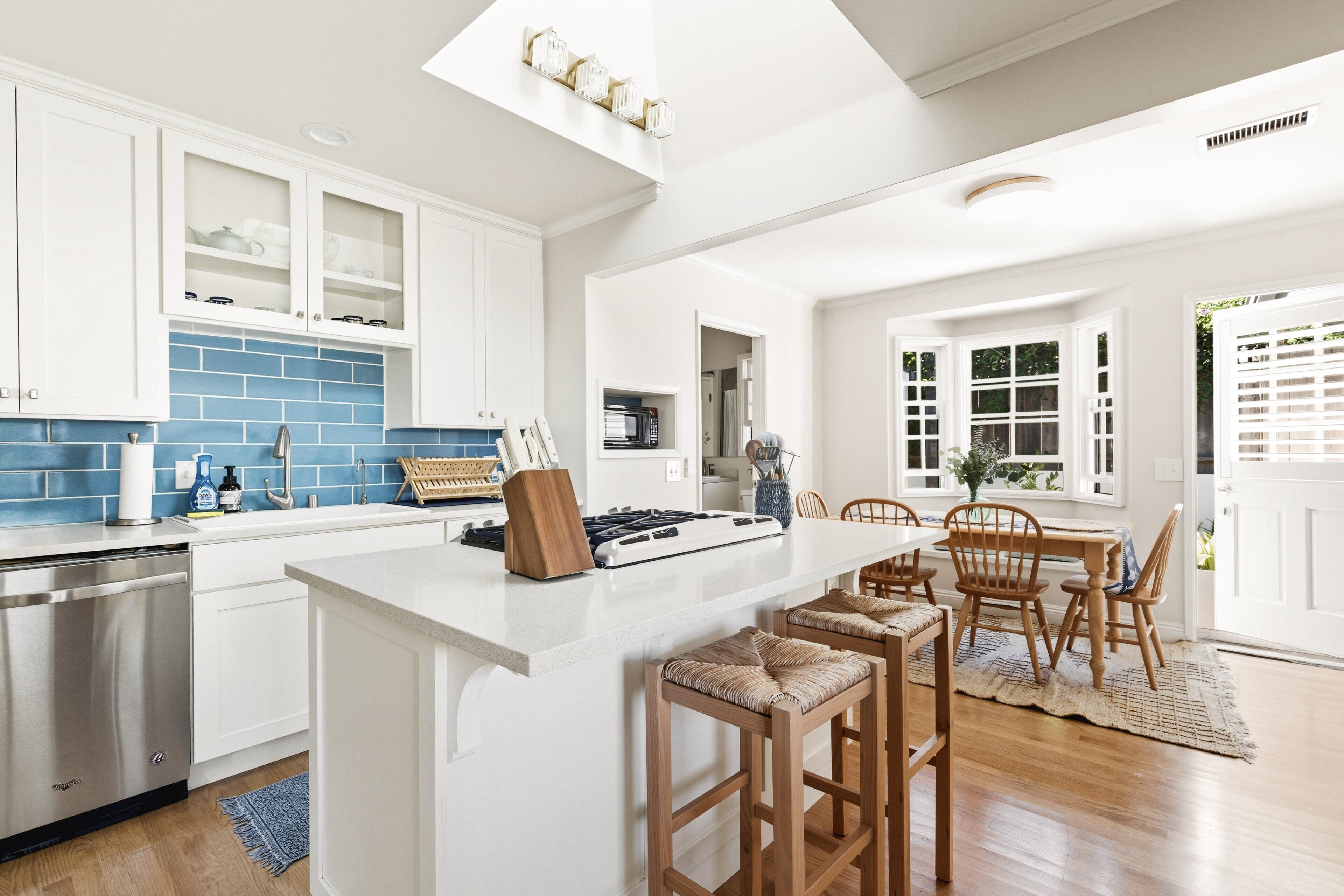 A modern kitchen with white cabinetry, a blue backsplash, and a central island with stools.