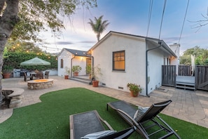 Um pátio com lareira, móveis de exterior e uma casa pequena com fachada branca.