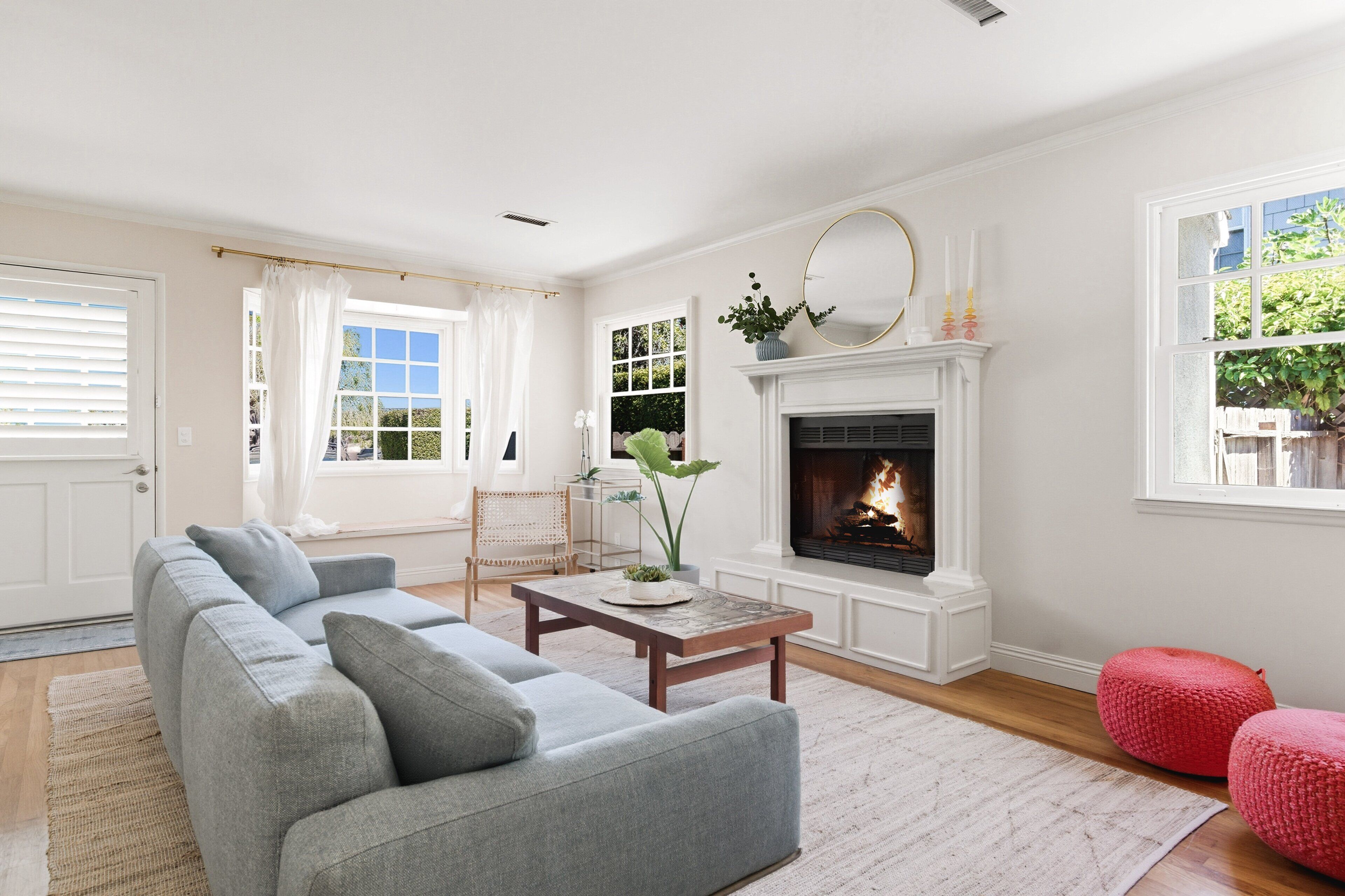 A living room with a fireplace, a sofa, a coffee table, and a red pouf.