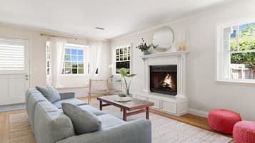 A living room with a fireplace, a sofa, a coffee table, and a red pouf.