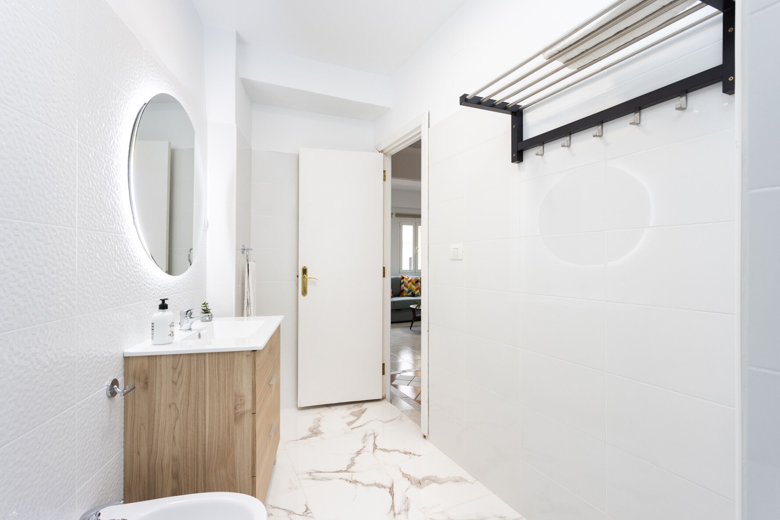 Ein modernes Badezimmer mit einem Holzbadschränkchen, einem runden Spiegel und einem gefliesten Boden in Weiß.