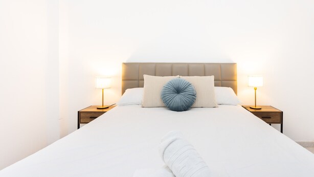 A neatly made bed with a headboard, two bedside tables with lamps, and a single decorative pillow.