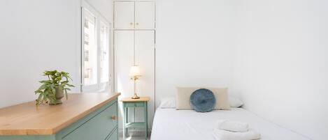 Een minimalistische slaapkamer met een bed, nachtkastje, lamp en een potplant.