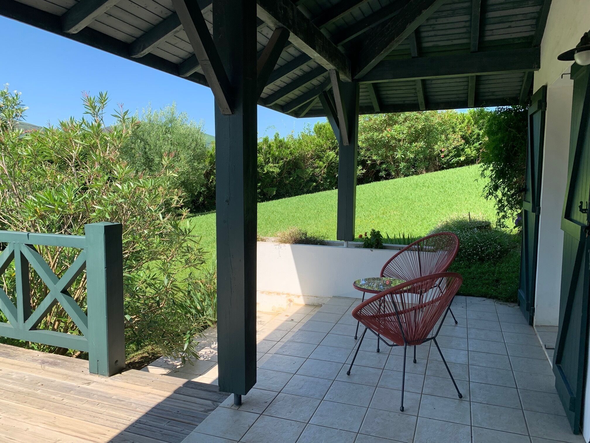 Une terrasse couverte avec une plateforme en bois, un portail vert et une chaise rouge.