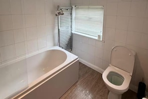 A bathroom with a bathtub, toilet, and a window with blinds. - Cottage - Sleeps 4 - Pets Ok - Garden - Parking (Middlewich)