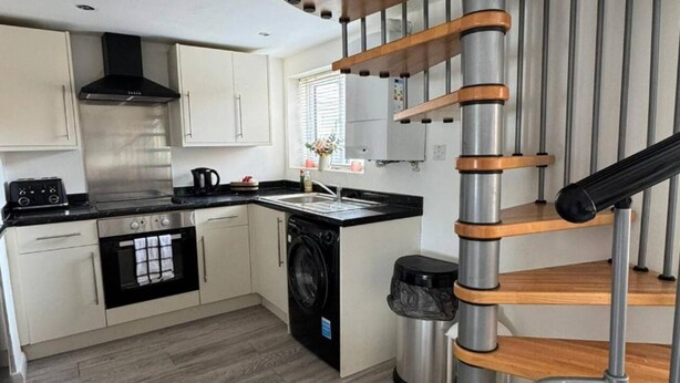 A modern kitchen with white cabinets, a black stove, and a stainless steel range hood.