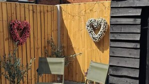 A wooden fence with heart-shaped decorations, two green chairs, and a small table.