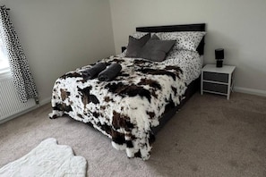 A bedroom with a bed, a nightstand, a lamp, and a polka dot curtain. - Cottage - Sleeps 4 - Pets Ok - Garden - Parking (Middlewich)