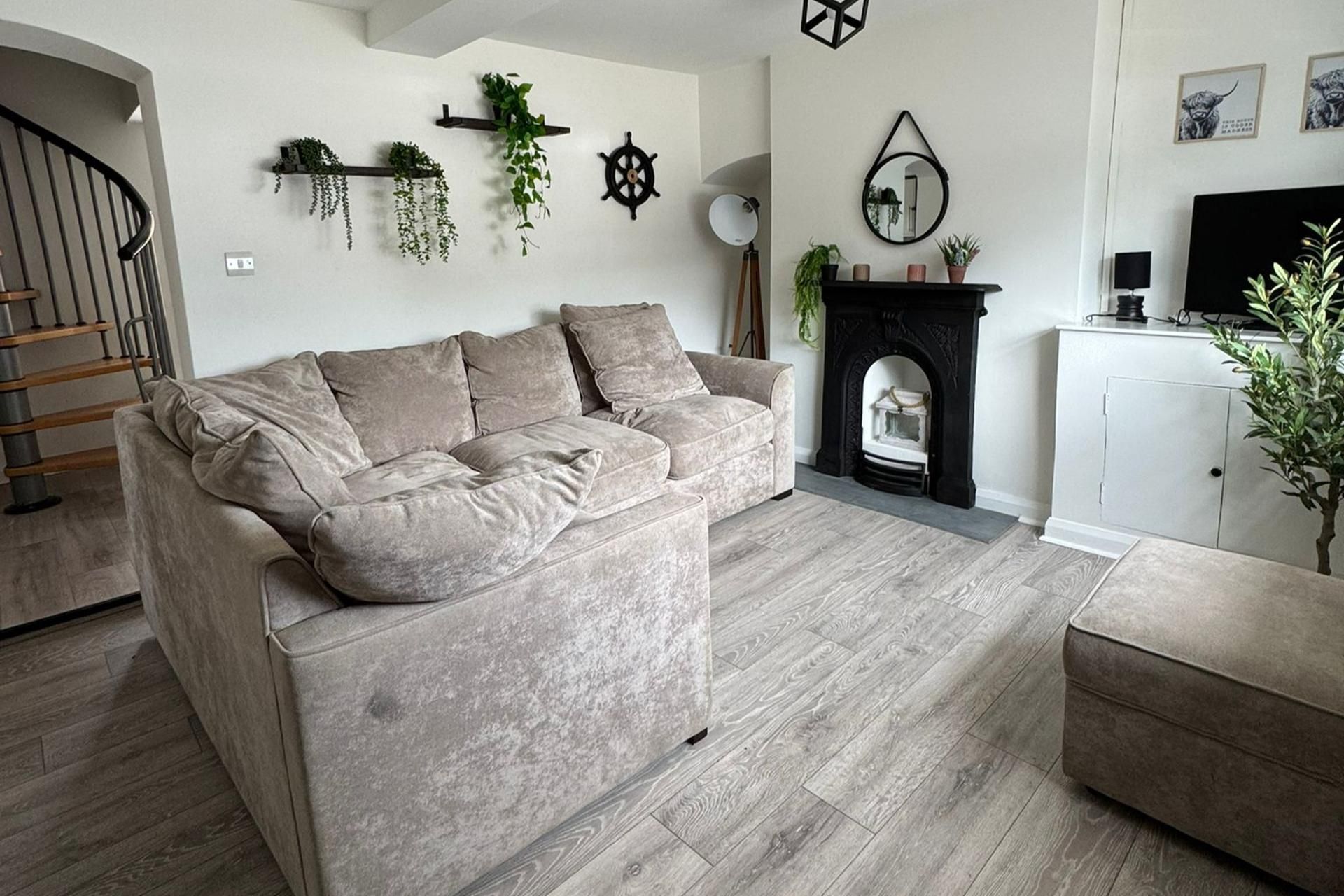 Una sala de estar con un sofá gris, una chimenea, un televisor y una escalera.