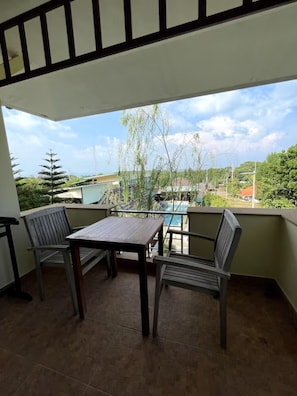 Un balcon avec une table et deux chaises, donnant sur une piscine et un espace verdoyant.