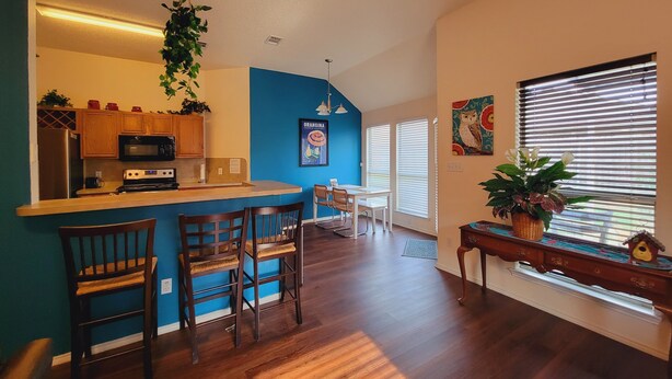 A modern kitchen with wooden cabinets, a bar area, and a dining space with a blue accent wall. - Private room in a Beautiful house Centrally Located  (Denton)