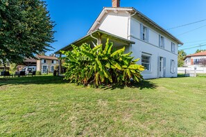 Una casa de dos pisos con fachada blanca, un porche cubierto y una palmera de plátano grande en el jardín delantero.