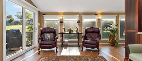 A spacious room with a ceiling fan, large windows, two leather chairs, a table with a vase, and a green chair.
