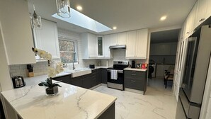 A modern kitchen with white marble countertops, dark cabinets, and a central island with a plant. - Tranquil Lakefront Cottage (Greater Napanee)