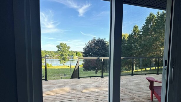 A wooden deck with a red bench, overlooking a lake and trees. - Tranquil Lakefront Cottage (Greater Napanee)