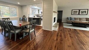 A modern living room with a wooden floor, a dining area with a table and chairs, a kitchen with white cabinets, and a fireplace. - Tranquil Lakefront Cottage (Greater Napanee)