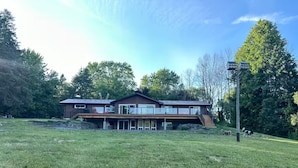 A modern two-story house with a large front porch, a garage, and a stone retaining wall. - Tranquil Lakefront Cottage (Greater Napanee)