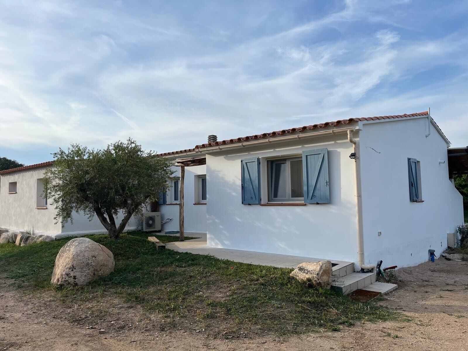 Un bâtiment blanc avec un toit en tuiles, un petit porche et un arbre devant.