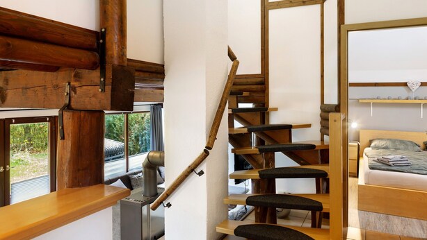 Una escalera de madera con barandilla, una cama con cabecera y una ventana con vistas al verdor.