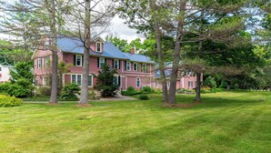 A large, two-story house with a red exterior and a blue roof, surrounded by a well-maintained lawn and several trees. - 3BR Riverfront Suite w/ Full Kitchen & Game Room (Intervale)
