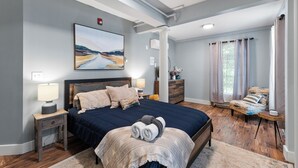 A bedroom with a large bed, a nightstand, a dresser, a chair, and a painting on the wall. - 3BR Riverfront Suite w/ Full Kitchen & Game Room (Intervale)