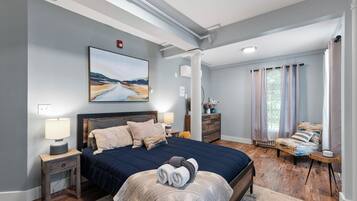 Een slaapkamer met een groot bed, een nachtkastje, een dressoir, een stoel en een schilderij aan de muur.