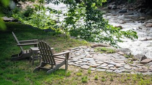 Un sentier de pierres menant à une rivière, bordé de verdure et agrémenté de deux fauteuils Adirondack.