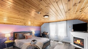 Une chambre avec un plafond en bois, un lit avec des oreillers, une table de chevet avec une lampe, une télévision et une cheminée.
