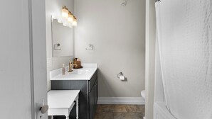 Een badkamer met een witte wastafel, een spiegel met verlichting, een toilet en een douchegordijn.